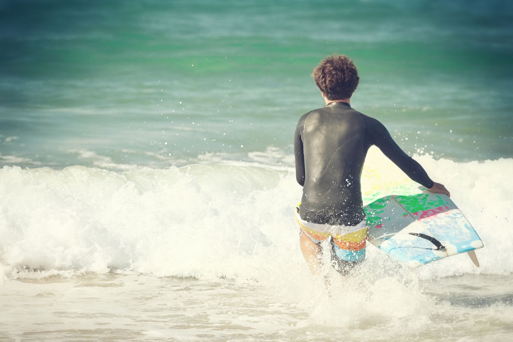 Surfer in a black long-sleeve rash top wading into breaking waves with a surfboard