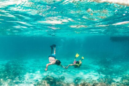 Two snorkelers swimming hand in hand over a shallow reef off Aruba