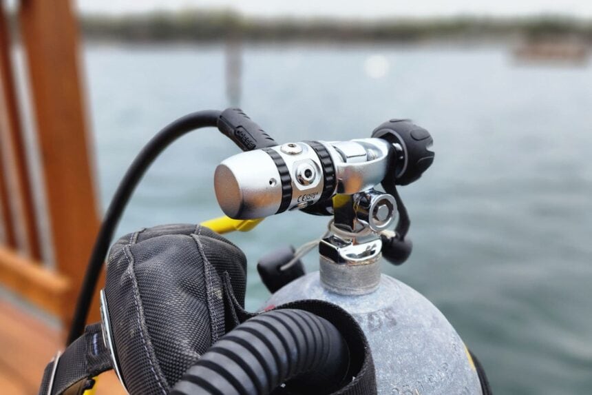 Cressi XS Compact AC2 first stage fitted to a tank on a dock with a quarry lake behind