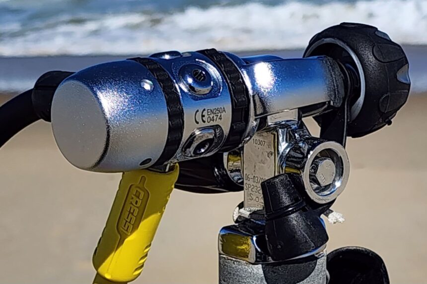 Close-up of the Cressi XS Compact AC2 first stage mounted on a tank valve with surf behind it