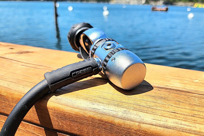 Cressi XS Compact AC2 first stage resting on a wooden rail above calm blue water