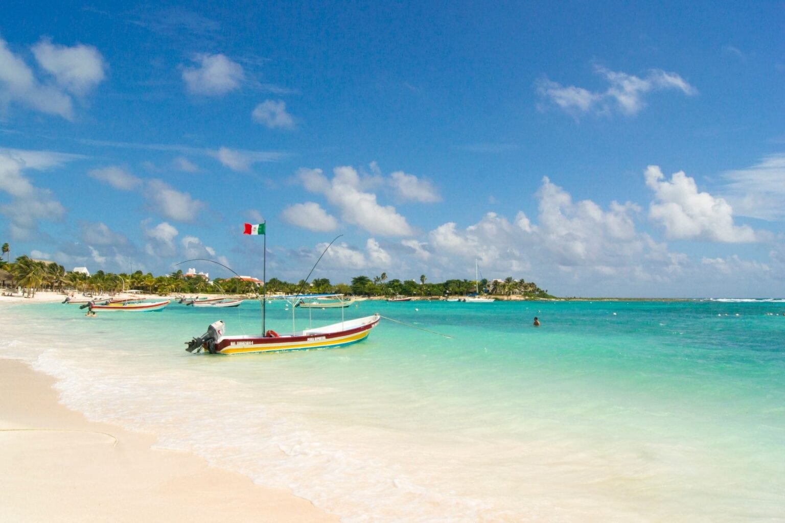 Yellow fishing boat anchored just offshore in the shallow turquoise water of a Riviera Maya beach