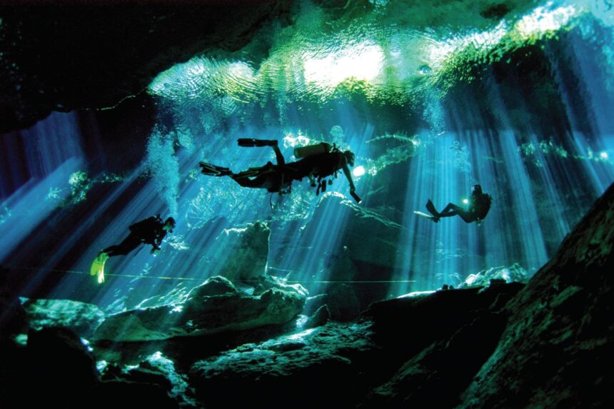 Divers silhouetted in sunbeams inside Dos Ojos cenote