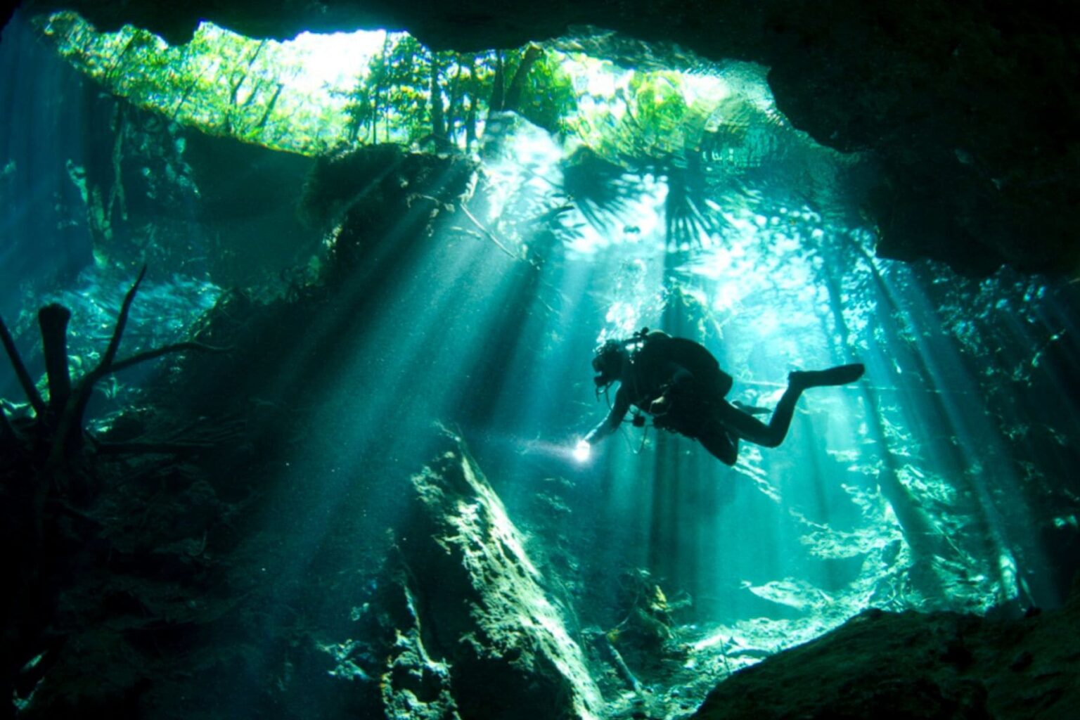 Diver descending through sunbeams inside a cenote cave system