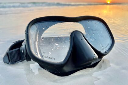 Oceanic Shadow frameless mask covered in water droplets, resting on wet sand at sunset