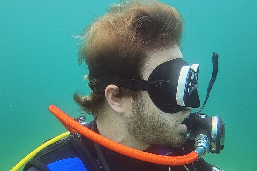 Side view of our tester underwater wearing the low-profile Mares Spyder while holding a camera