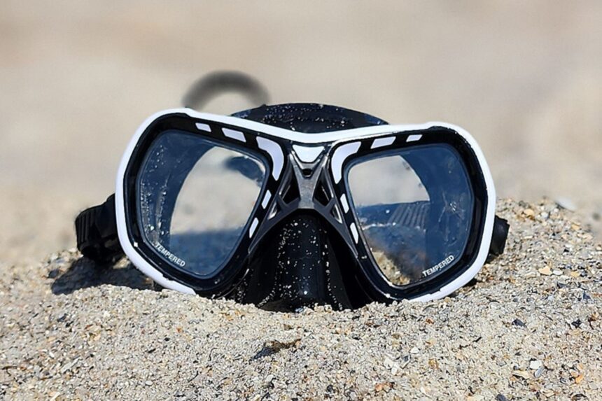Mares Spyder twin lens mask half buried in beach sand, seen straight on