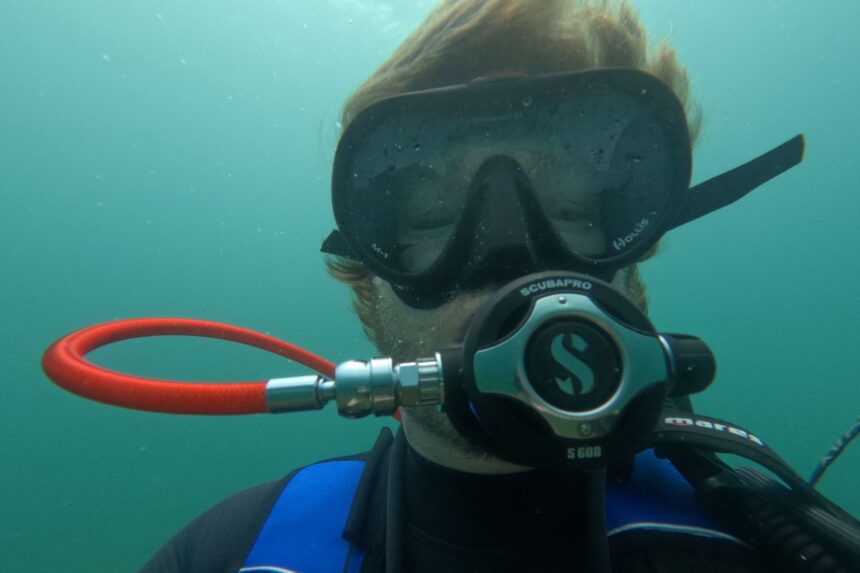 Straight-on view of our tester underwater wearing the Hollis M1 in green coastal water