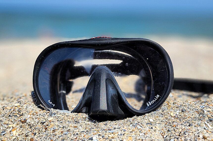 Hollis M1 mask half buried in beach sand with the sea blurred behind it