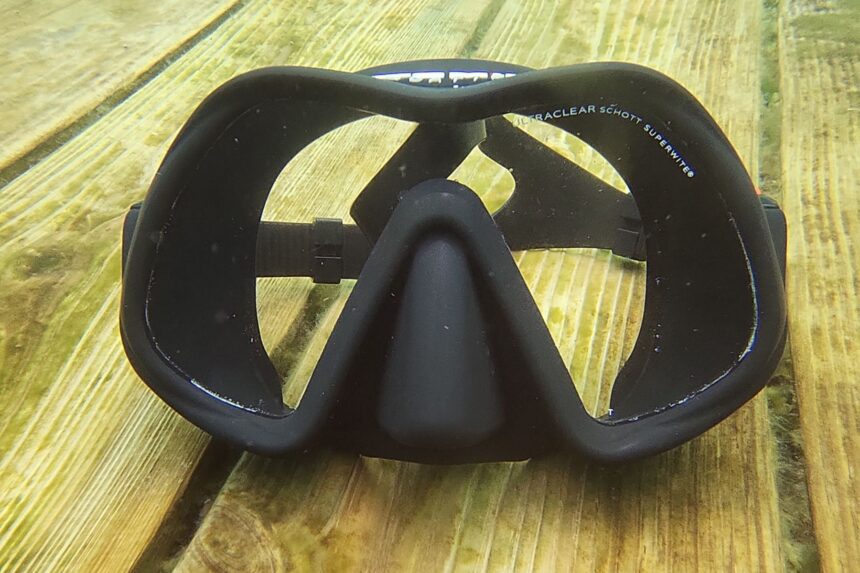 Atomic Aquatics Venom lying lens up on wet planks with Ultraclear Schott glass marked on the lens