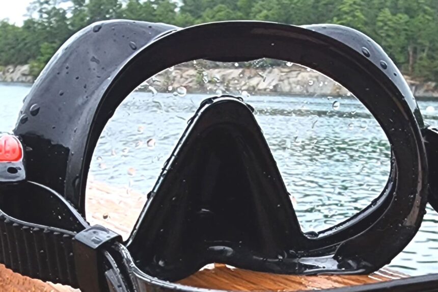 Close-up of the Atomic Aquatics Venom mask face seal beaded with water beside a rocky shoreline