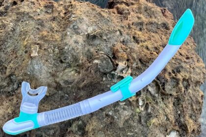Mares Ergo Splash snorkel in clear and teal resting on a pale rock above the water