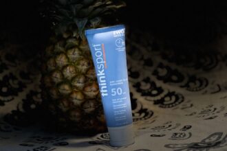 Thinksport SPF 50 clear zinc sunscreen tube standing in front of a pineapple in dim light