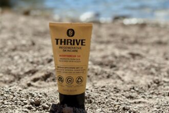 Thrive Regenerative Skincare BodyShield 50 tube standing upright in gravel at the water's edge