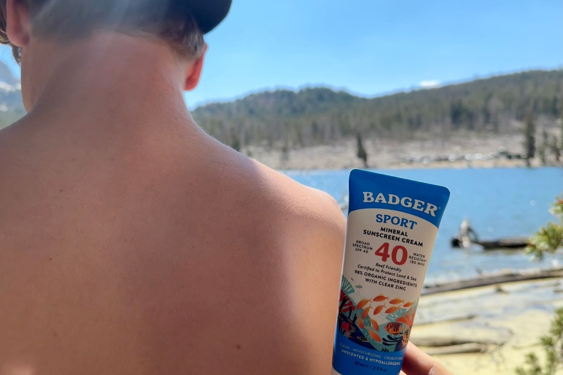 Our tester holding the Badger Sport tube beside bare shoulders at a mountain lake