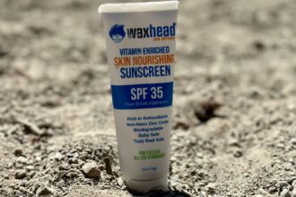 Waxhead Sun Defense SPF 35 sunscreen tube standing in dry sand and gravel