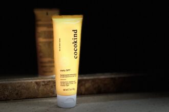Cocokind daily SPF 32 facial sunscreen lotion tube on a stone ledge in low light