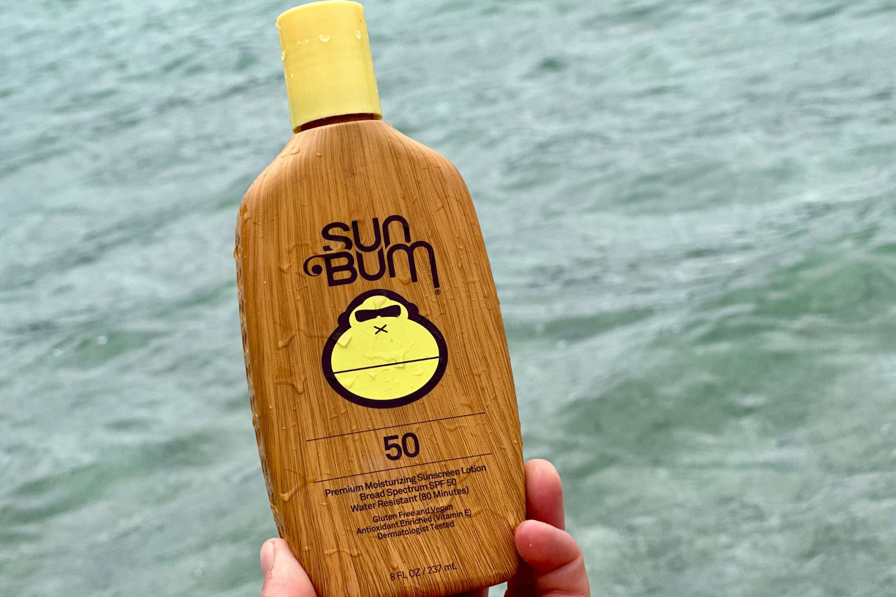 Wet Sun Bum Original SPF 50 lotion bottle held up in front of choppy water