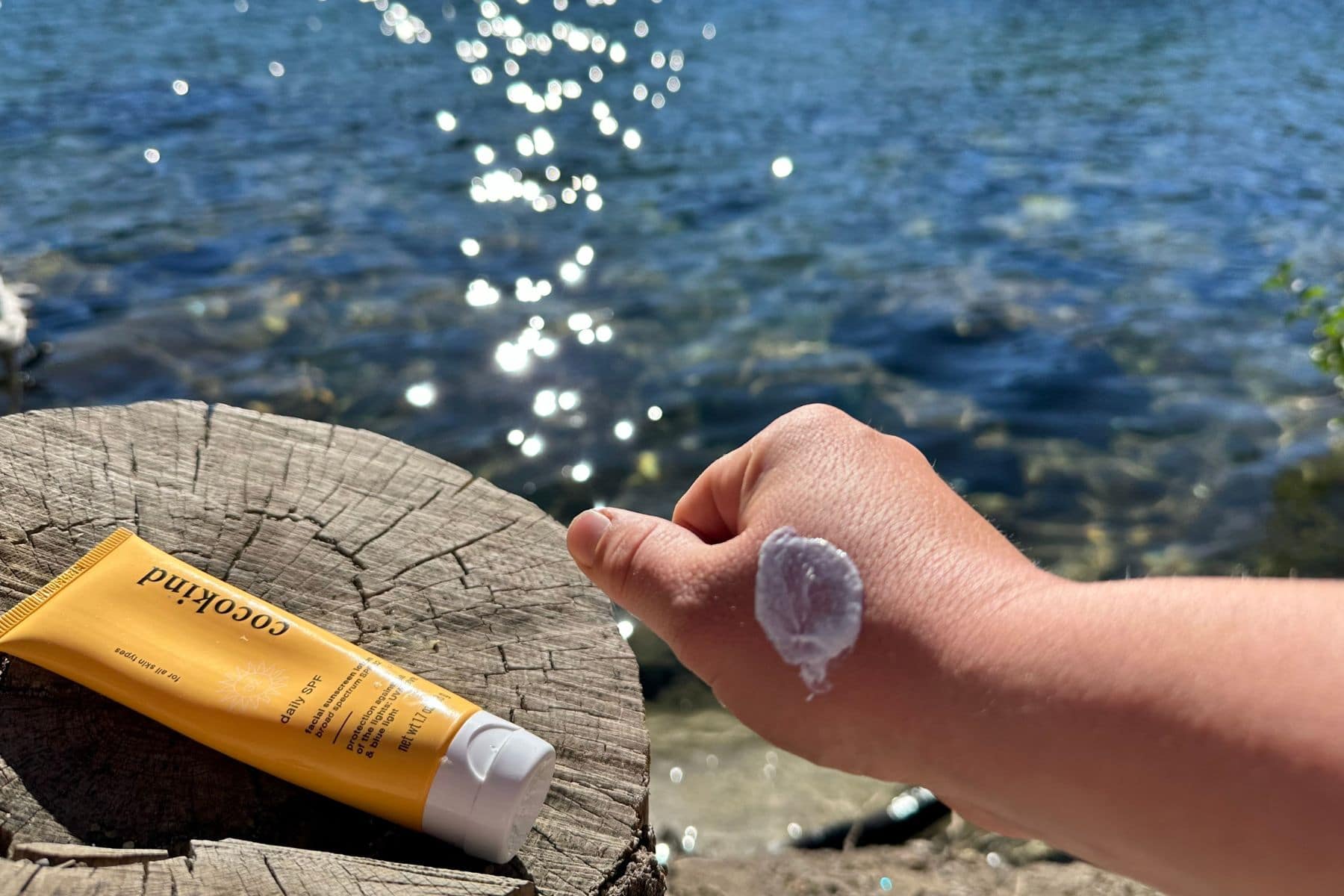 Blob of Cocokind daily SPF lotion on a tester's hand with the tube resting on a stump