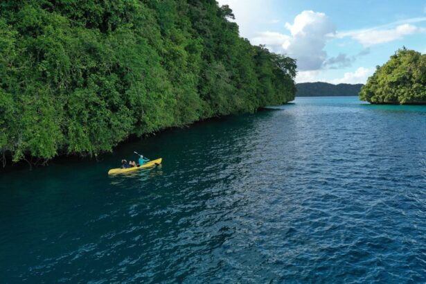 Two guests paddling a yellow kayak through calm water beneath Palau's forested rock islands