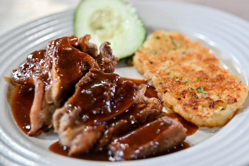 Sauced meat with cucumber and a hash brown patty on a dinner plate aboard the ship