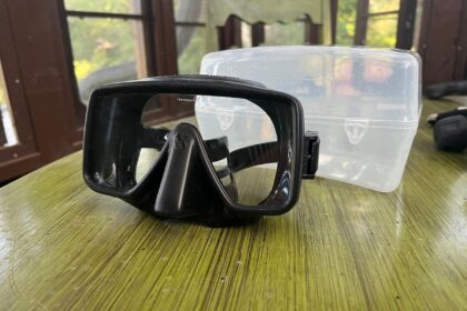 ScubaPro Gorilla frameless dive mask with a single black lens resting on a table beside its clear case