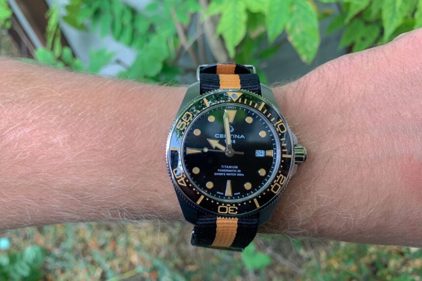 Certina DS Action Diver on a wrist with a black and orange NATO strap, greenery behind