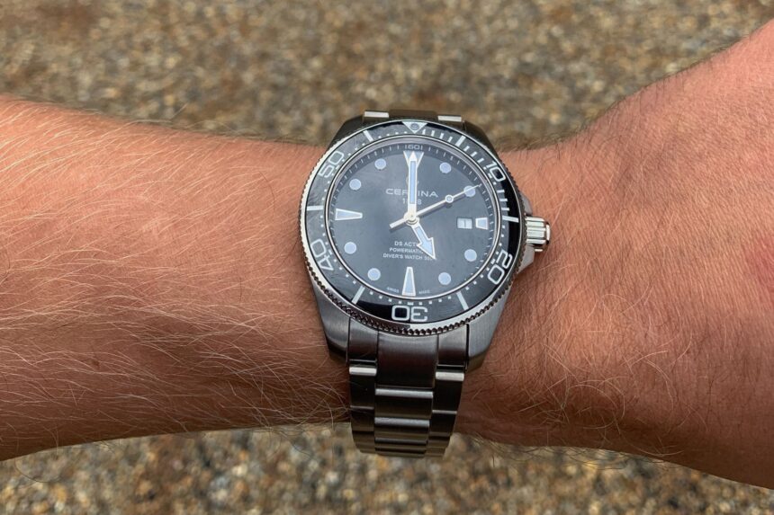 Certina DS Action Diver with black dial and steel bracelet worn on a wrist over gravel