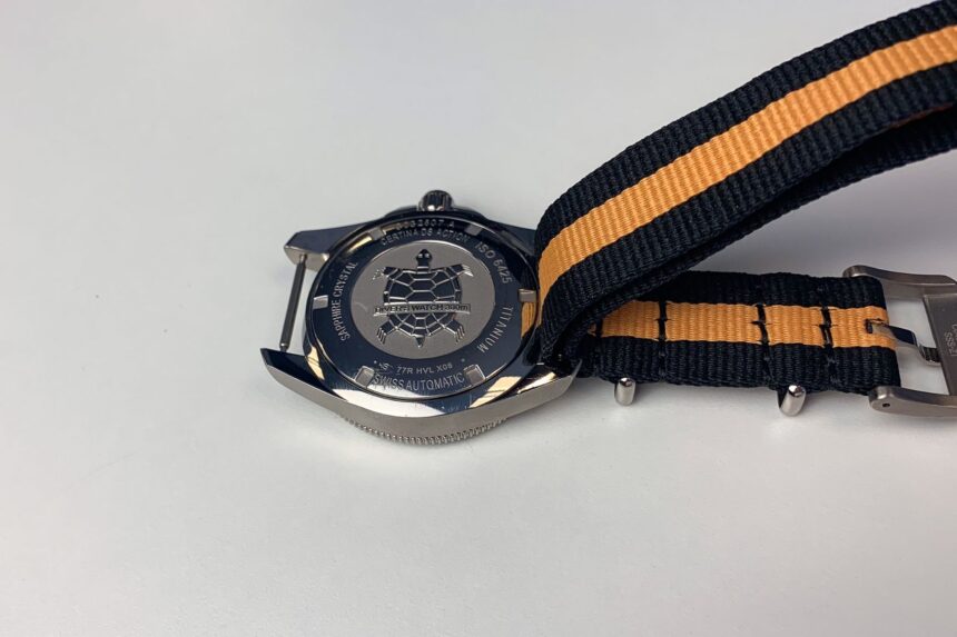 Certina DS Action Diver case back beside its black and orange NATO strap and buckle