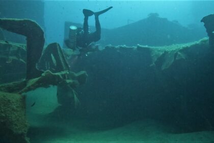 Diver finning upside down over the encrusted deck of a wreck in Malta