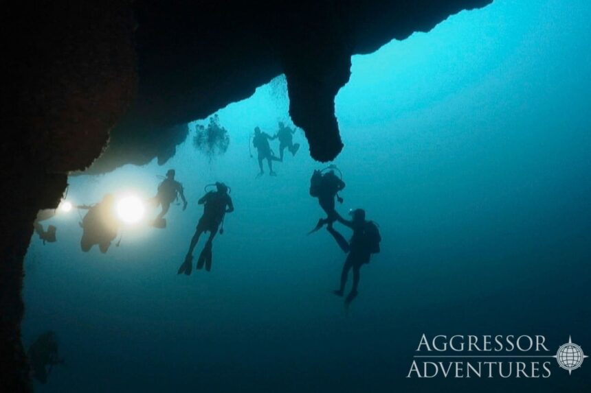 Divers silhouetted beneath a rock overhang in the deep blue of the Great Blue Hole in Belize