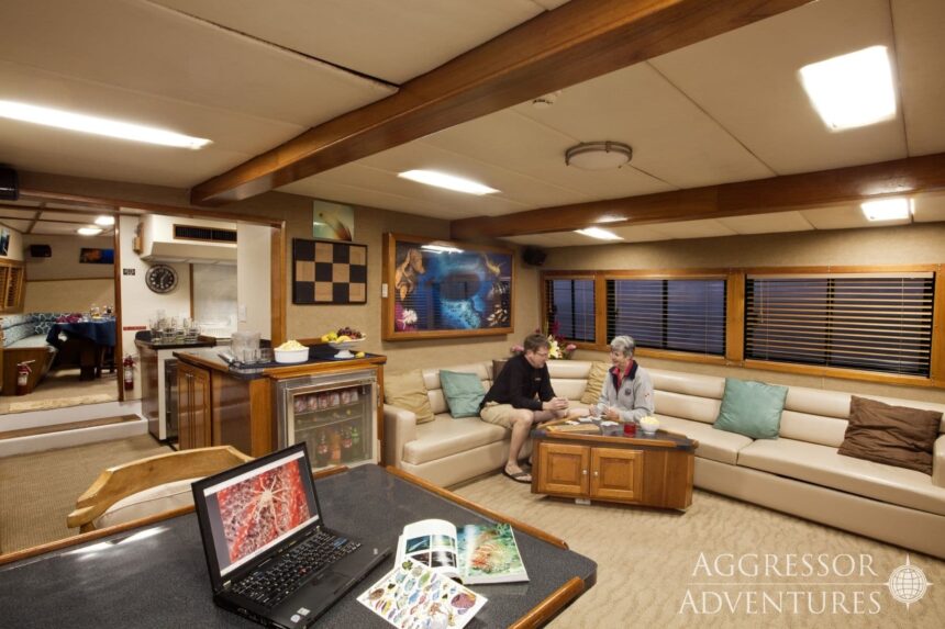 Guests relaxing in the wood paneled salon lounge aboard the Belize Aggressor III