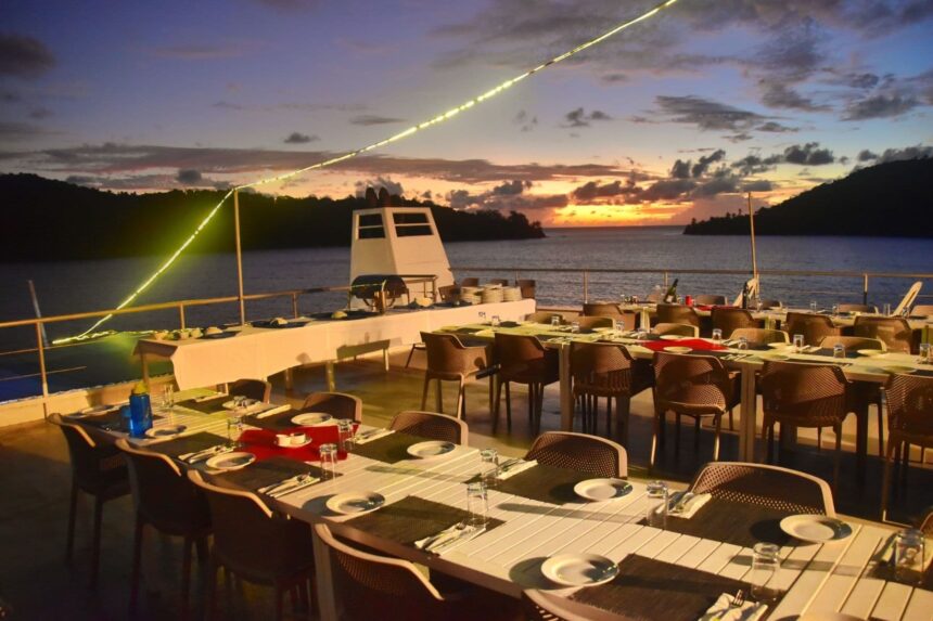 Dining tables set on deck as the sun sets over Fiji