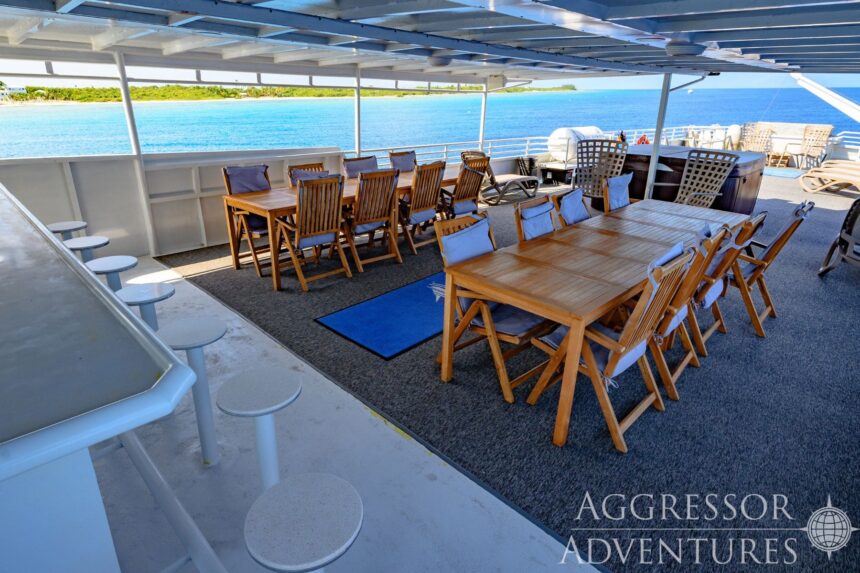 Wooden dining tables set up on the covered deck of the Cayman Aggressor IV overlooking the sea
