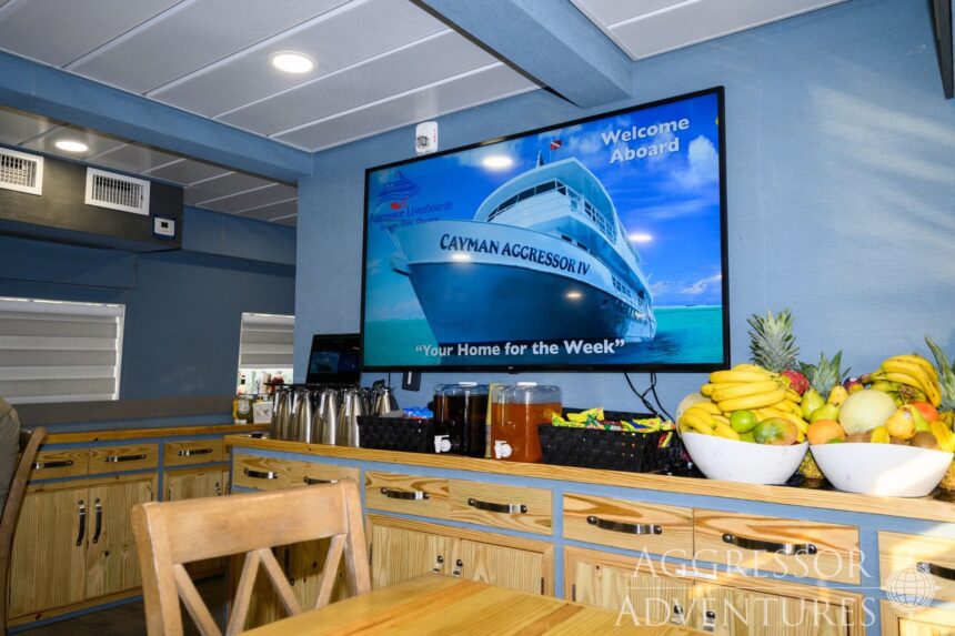 TV screen welcoming guests aboard the Cayman Aggressor IV beside bowls of fresh fruit at the buffet