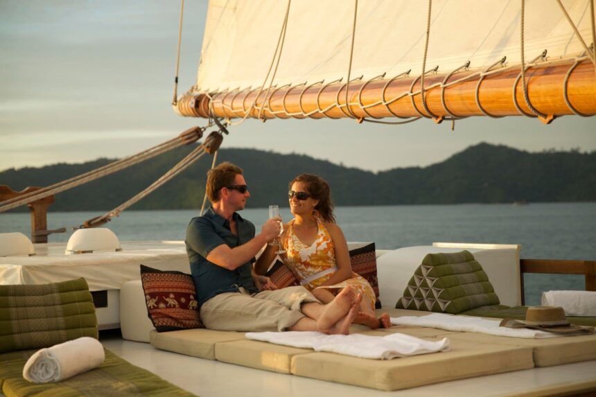 Couple relaxing with drinks on cushions at sunset aboard the Emperor Raja Laut