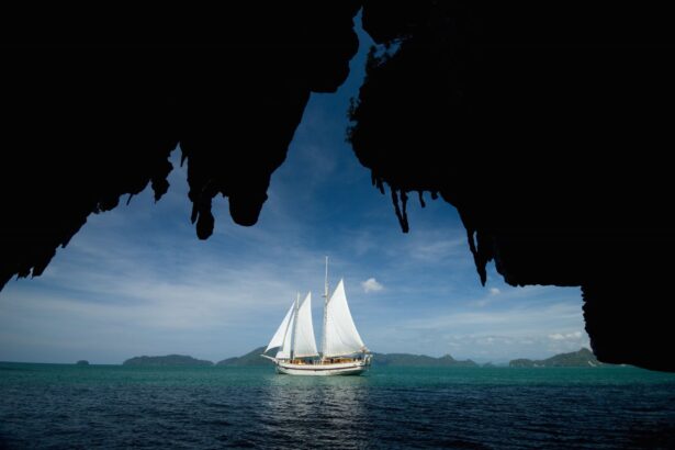 Emperor Raja Laut sailing under white sails framed by a limestone cave opening