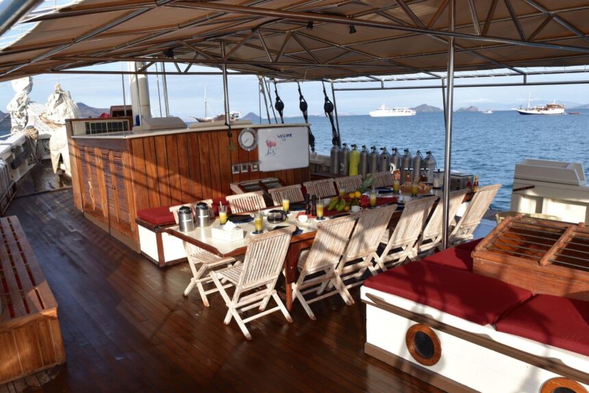 Breakfast table set on the covered deck of the Emperor Raja Laut with hills in the background