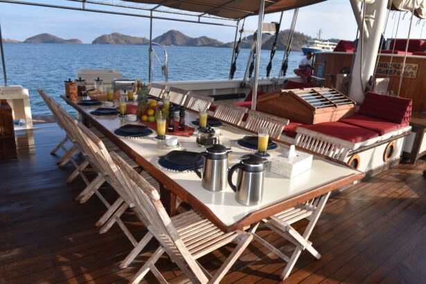 Breakfast table set on the covered deck of the Emperor Raja Laut with coastal hills beyond