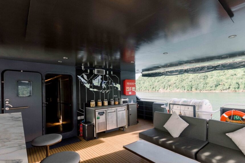 Covered outdoor lounge on the All Star Velocean with sofas facing a wooded shoreline