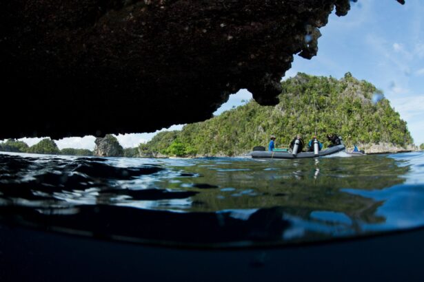 Divers boarding a skiff near limestone islands, seen from the waterline through a cave opening