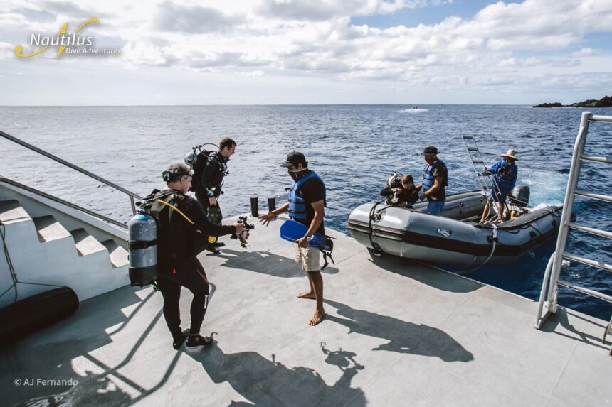 Divers gearing up on deck while a skiff waits alongside for pickup