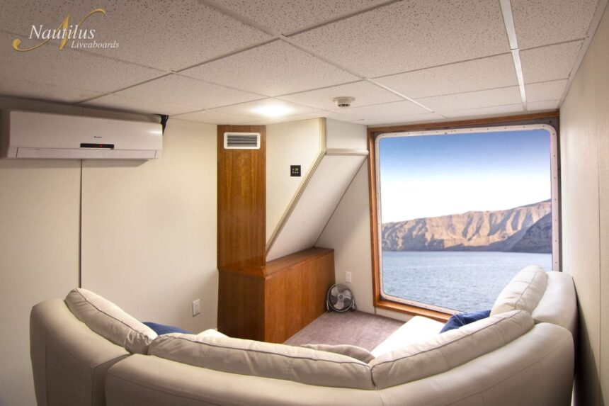 Lounge cabin aboard the Nautilus Explorer with a corner sofa and ocean-view window