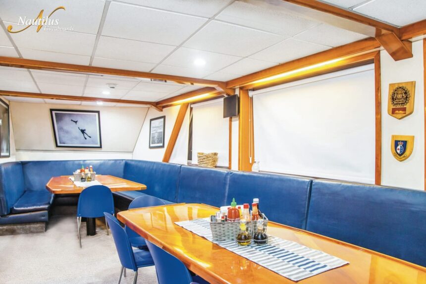 Dining lounge aboard the Nautilus Explorer with blue booth seating and wooden tables