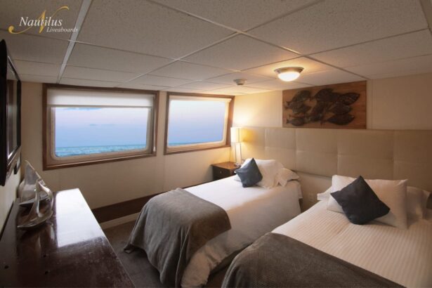 Twin bed cabin aboard the Nautilus Explorer with ocean-view windows and a mounted TV