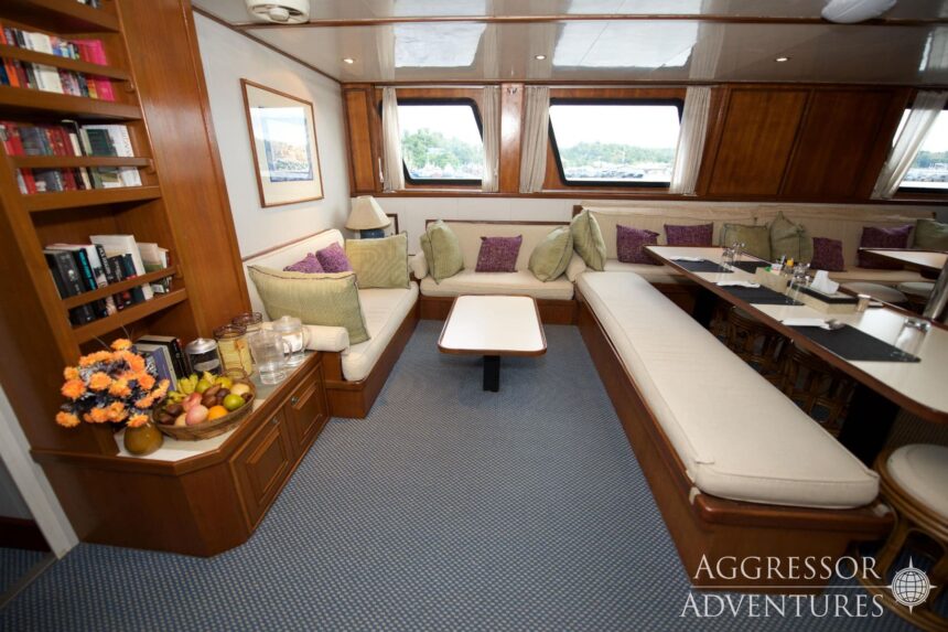 Wood paneled salon lounge with sofas and dining tables aboard the Raja Ampat Aggressor