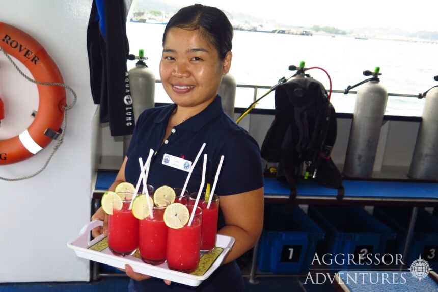 A crew member serves red juice drinks on deck near dive tanks aboard the Raja Ampat Aggressor