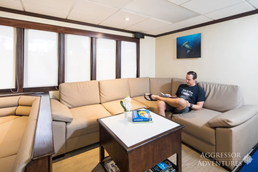Guest relaxing with a book on the sofa aboard the Okeanos Aggressor II