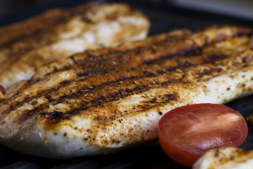 Close-up of a grilled fish fillet with charred grill marks and a halved tomato