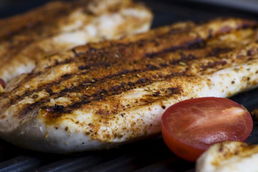 Close-up of a grilled fish fillet with charred grill marks and a halved tomato